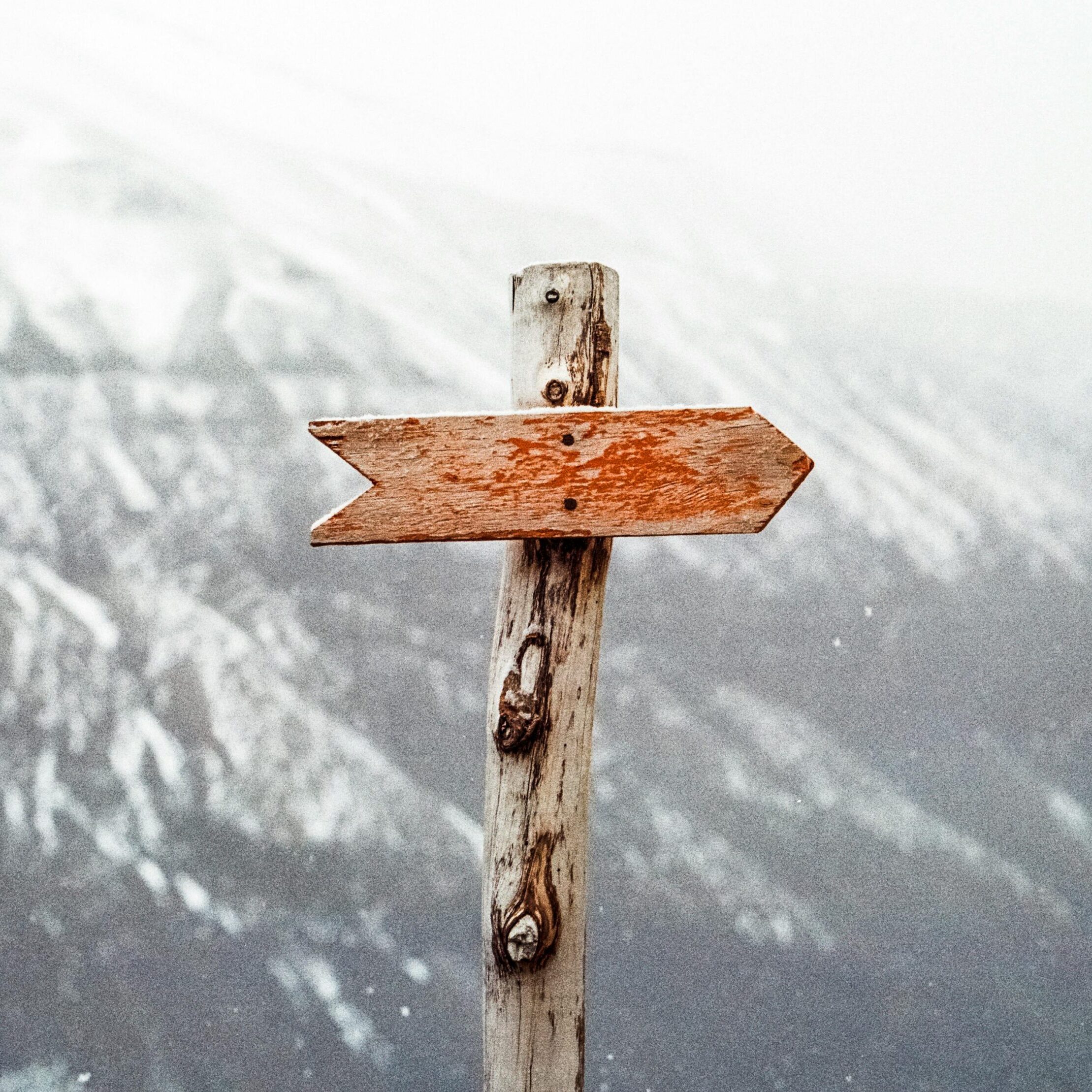 A wooden arrow signpost points the way amidst a snowy mountain landscape.